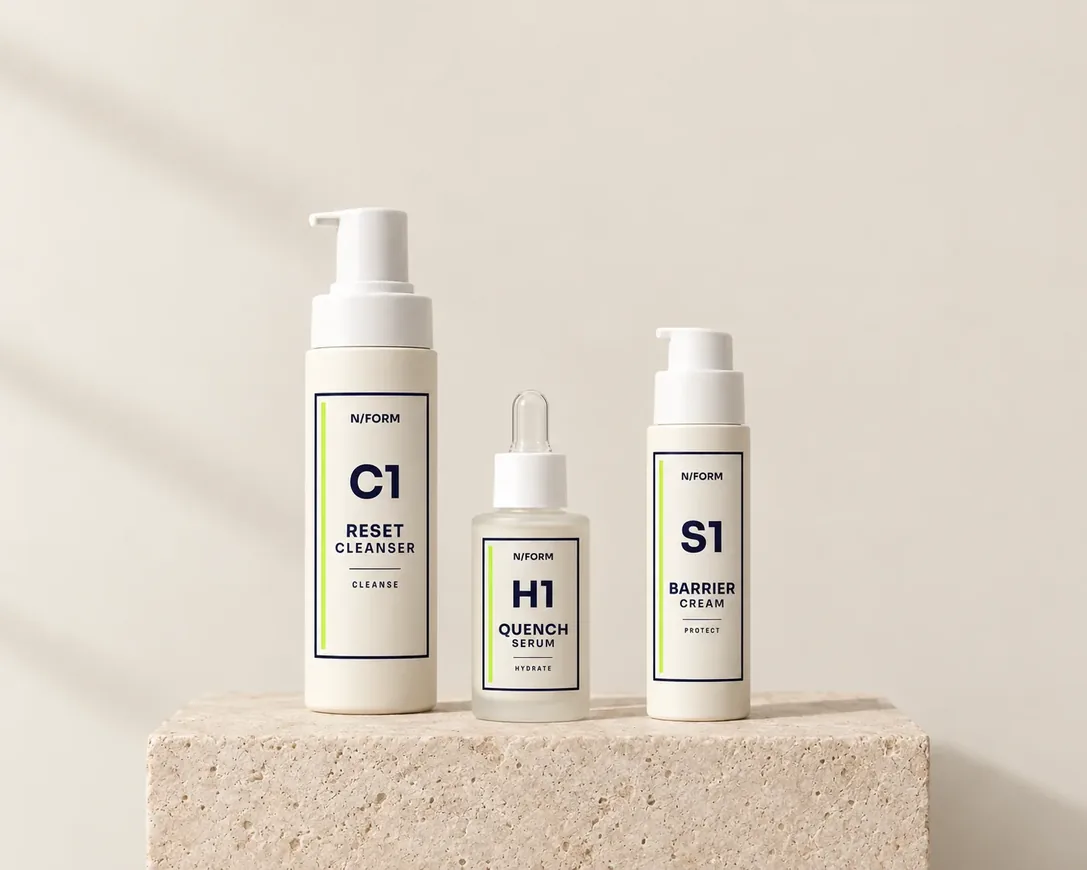 Three N/FORM bottles on a travertine plinth: a cleanser, a serum and a cream